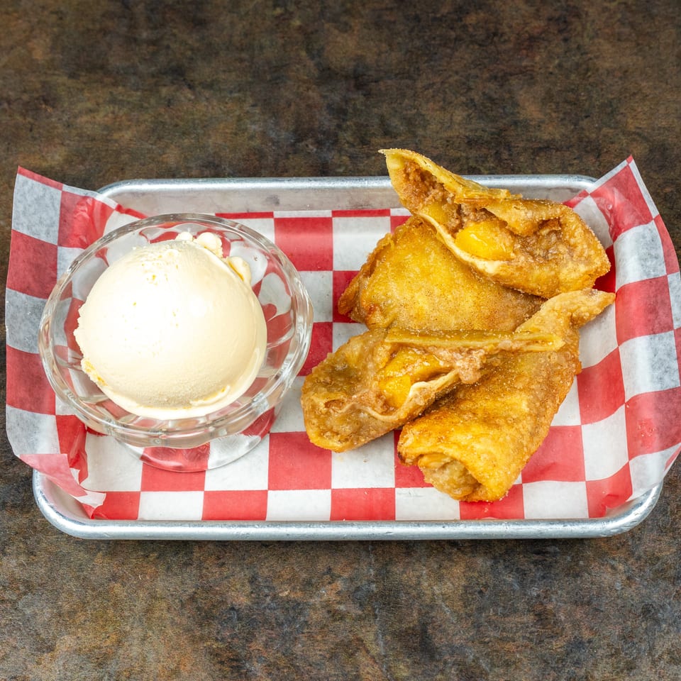 Crispy fried empanadas filled with meat and cheese served with a scoop of vanilla ice cream on a checkered-lined tray.