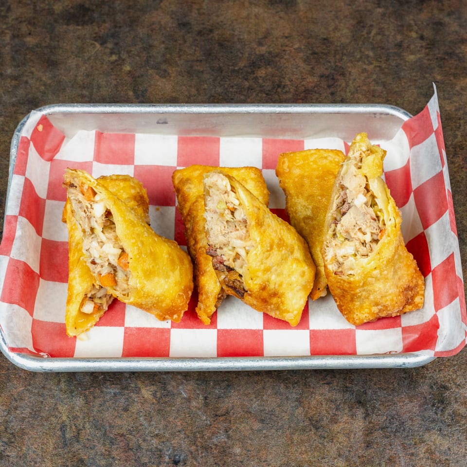 Golden fried stuffed pastries filled with shredded meat and vegetables in a red-and-white checkered basket liner.